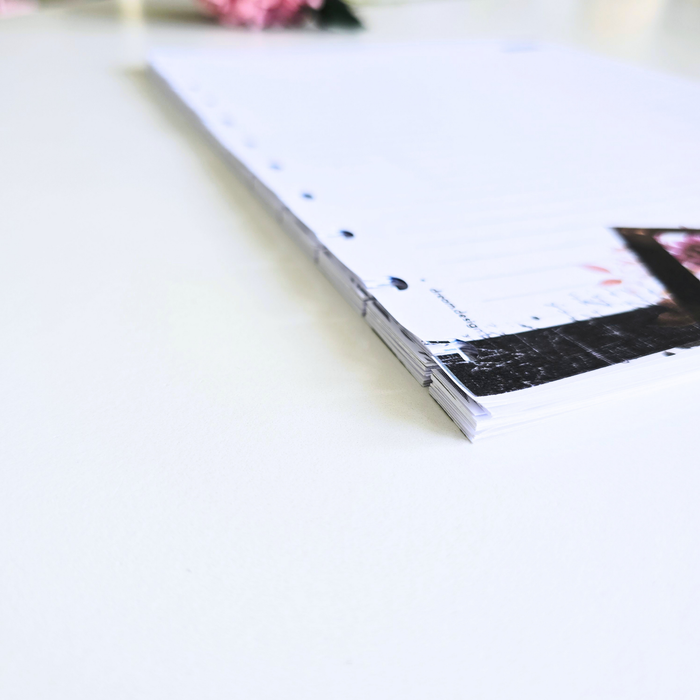 A close-up of discbound notes pages
with lined writing space, shown on a clean white surface. The binding is pale pink, and part of a printed page design with a dark rectangular photo insert is visible.