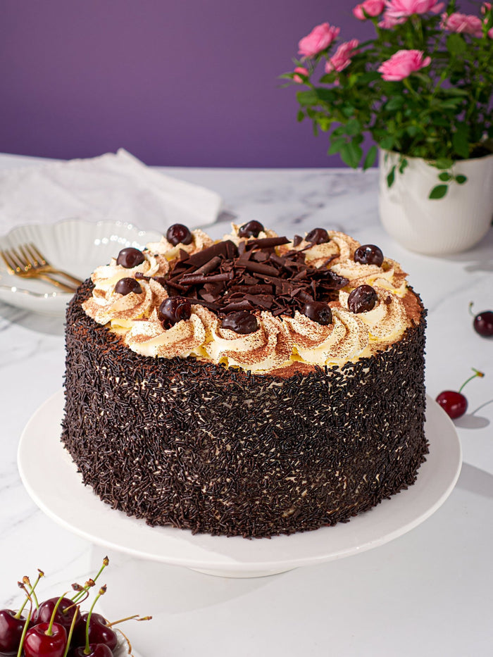 Black Forest Gateau coated in chocolate flakes and topped with cream swirls, cherries and chocolate curls