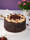 Black Forest Gateau coated in chocolate flakes and topped with cream swirls, cherries and chocolate curls