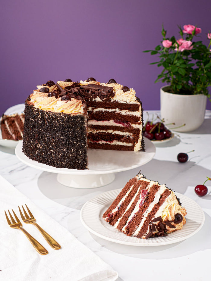 Black Forest Gateau cut open to show its cherry and cream sponge layers, with a slice plated in front