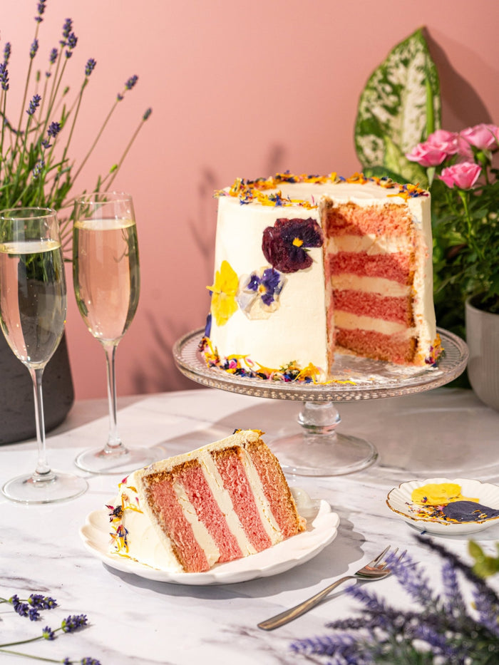 Elderflower and rose cake cut to show its pink and white sponge layers, a slice plated in front