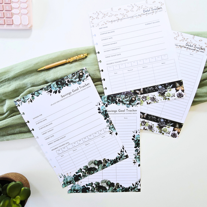 A styled flat-lay of several printed budget and savings goal tracker sheets with floral greenery borders, arranged on a white surface with a folded sage green cloth, a gold pen, a small plant, and part of a pink calculator visible. Disc Bound Planner. Discbound