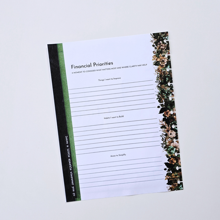 A flat-lay view of a 'Financial Priorities' notepad on a light gray background. The notepad has a white writing surface with lined sections, a black spine band with green and white text, and a floral border on the right side. Disc Bound Planner. Discbound