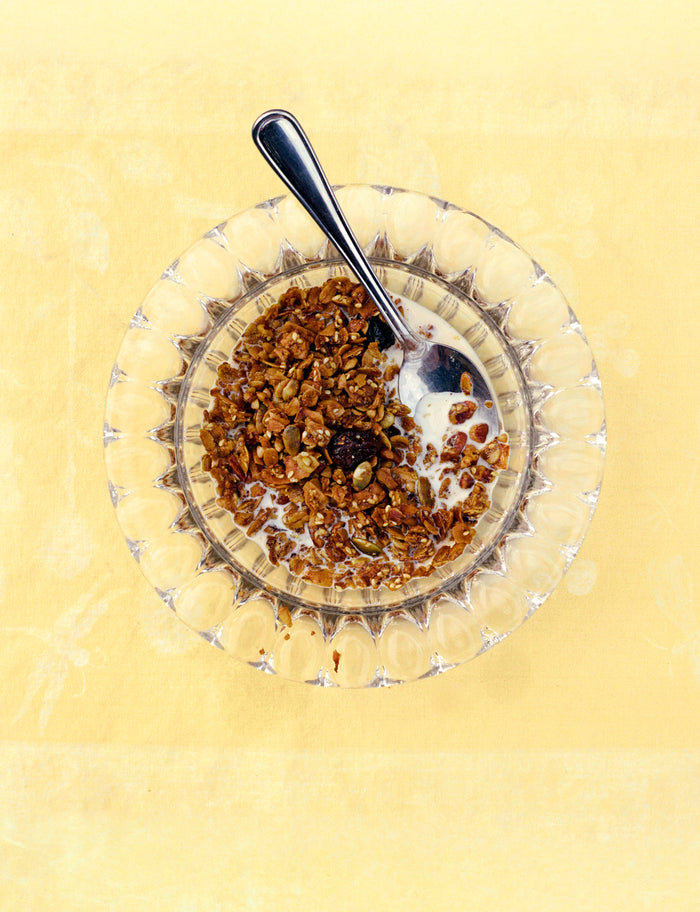 Glass bowl with granola and milk on a yellow background