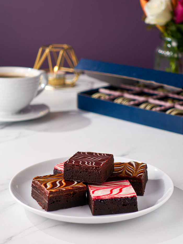 Four Patisserie Valerie chocolate fudge brownies on a plate beside a coffee, with the birthday brownie gift box behind
