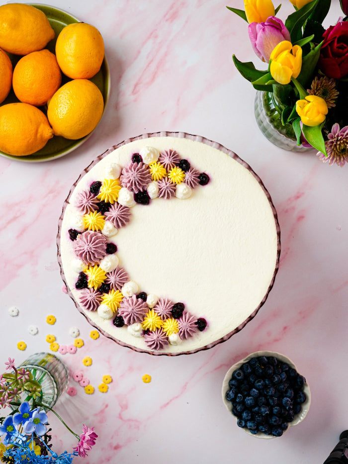 Overhead view of the lemon and blueberry cake, a crescent of piped cream and blueberries on top