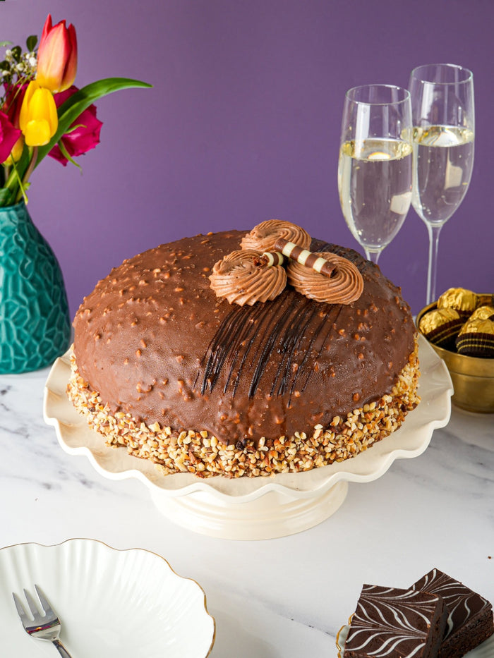 Whole Nutella crunch dome cake on a cake stand beside two glasses of champagne