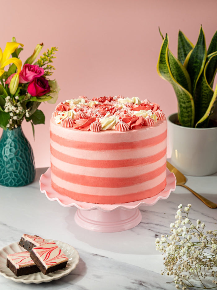 Pink Candy Stripe Gateau on a pink cake stand with fresh flowers and a plate of brownies