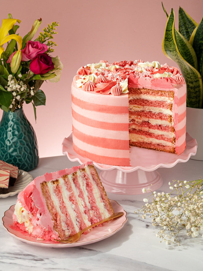 Pink Candy Stripe Gateau cut open to show its pink sponge and vanilla cream layers, slice plated in front