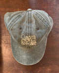 A green baseball hat with an abstract floral design and text on the front, displayed on a wooden surface.