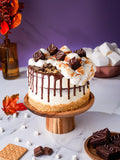 S'mores Cake with toasted marshmallow, chocolate drip and brownie pieces on a biscuit crumb base