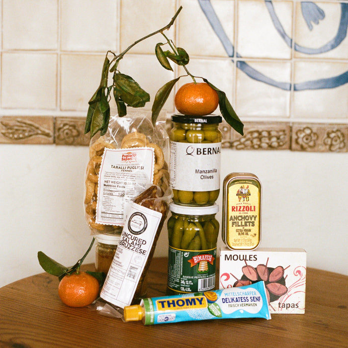 Assorted food products including jars, a box, and a bag on a wooden surface with a tiled wall background.
