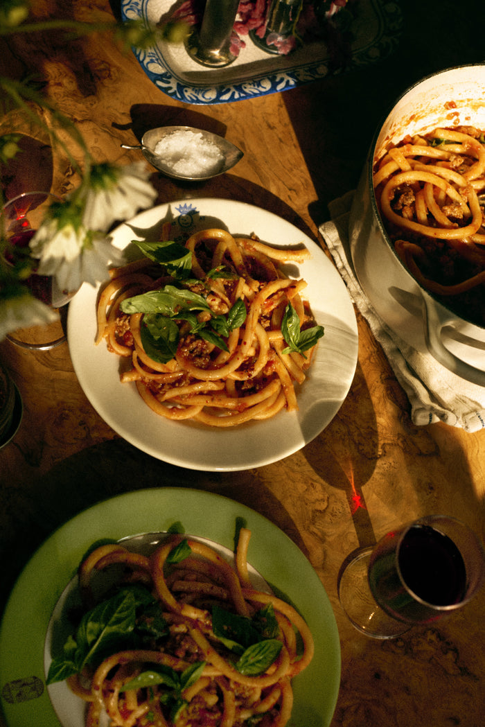 Plates of pasta with greens on a wooden table with glasses and a candle.