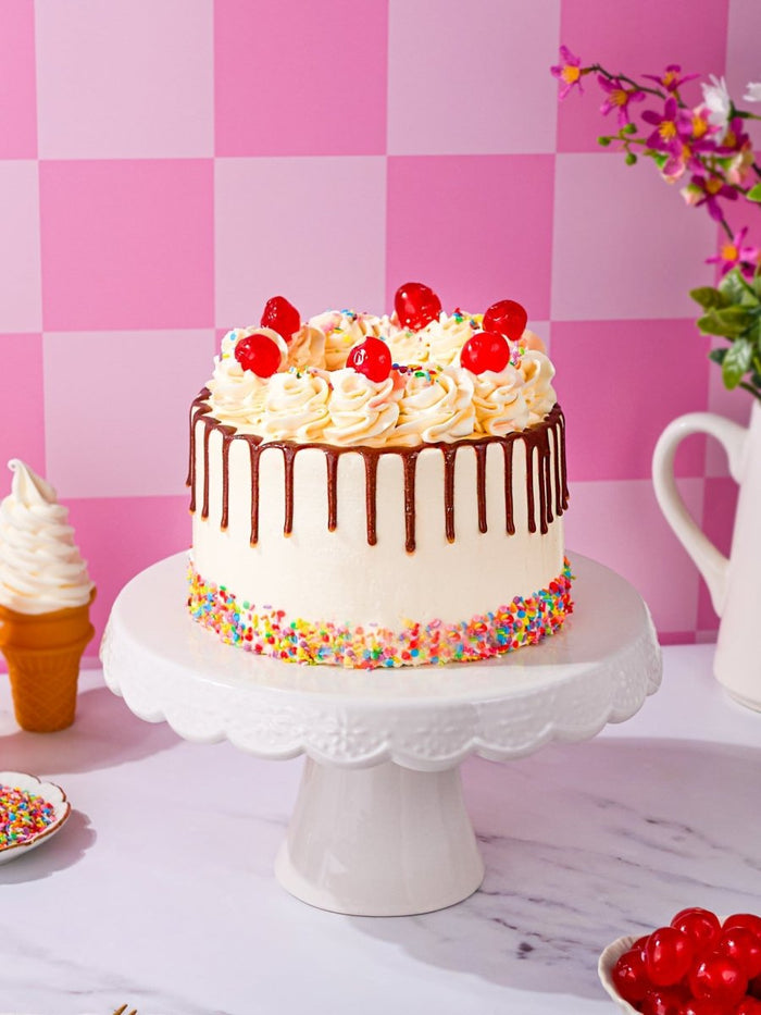 Sweet Treat Sundae Cake with chocolate drip, glace cherries and a band of rainbow sprinkles