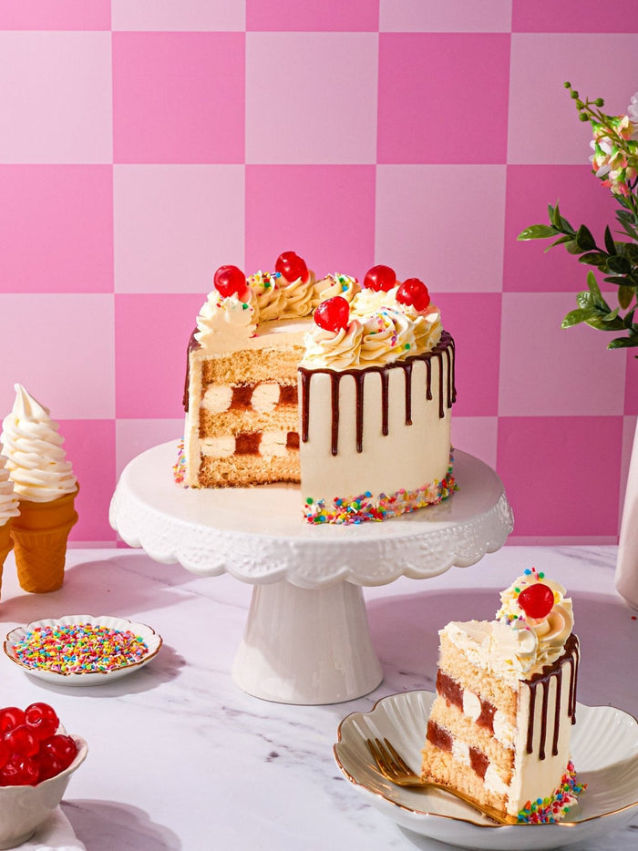 Sundae cake with a wedge cut away and a slice on a plate beside a bowl of cherries