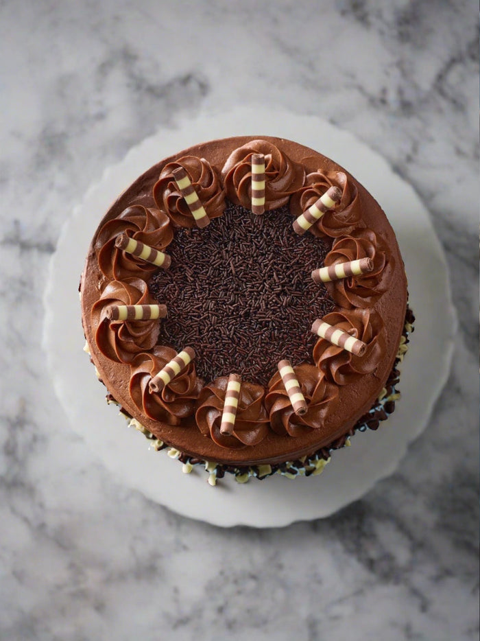 Overhead view of the chocolate layer cake, sprinkle centre ringed with rosettes and chocolate cigarillos