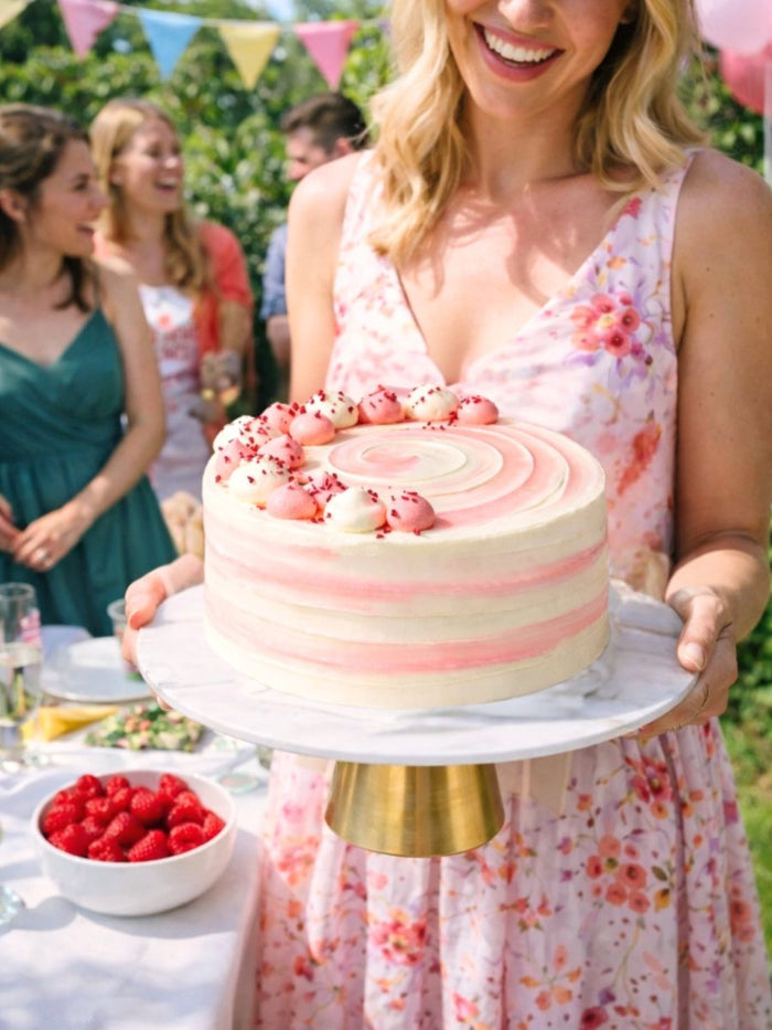 Woman carrying a raspberry ripple celebration cake to a garden party table