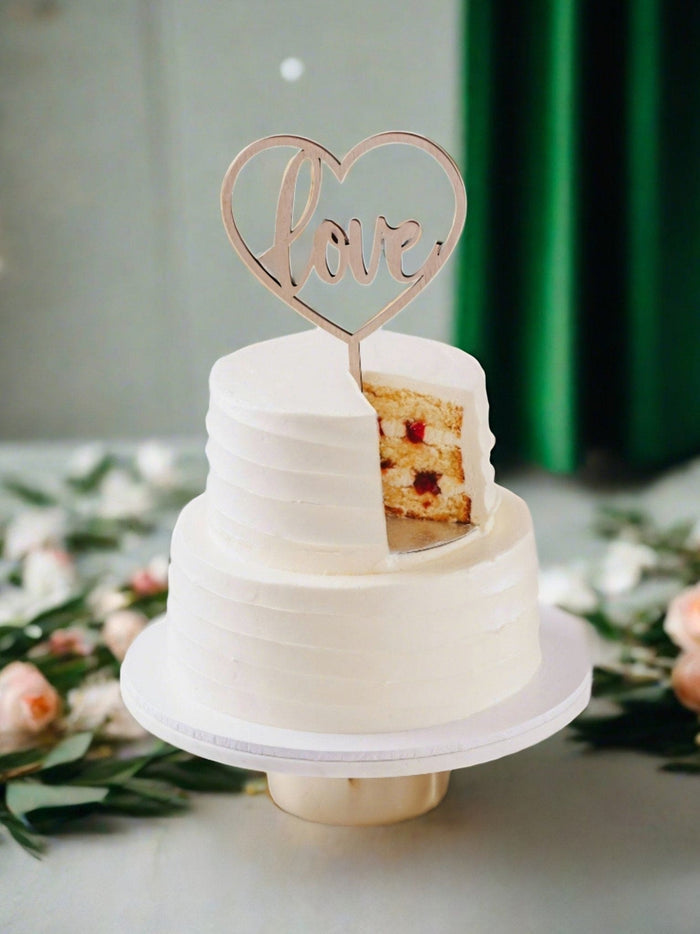 Vanilla two tier wedding cake with a love topper and a wedge cut to reveal the strawberry filling