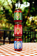 Three jars of tomato sauce stacked on a checkered tablecloth with a blurred green outdoor background