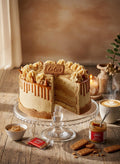 Vegan Biscoff Cake cut open on a glass stand with caramel drip, a Lotus biscuit and a coffee alongside
