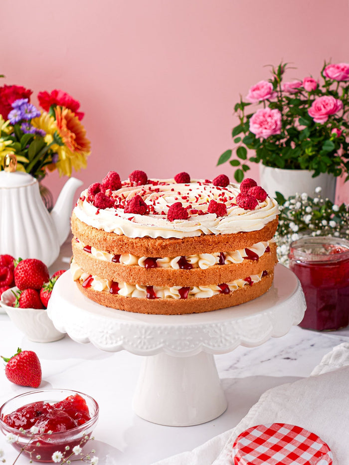 Victoria sponge on a cake stand with a jar of strawberry jam and fresh strawberries beside it
